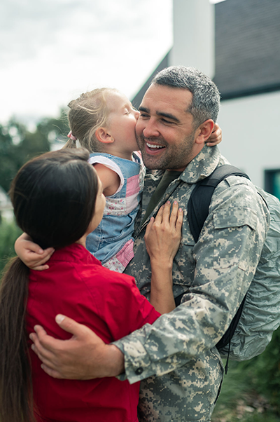 Military father receiving kiss from daughter held by mother